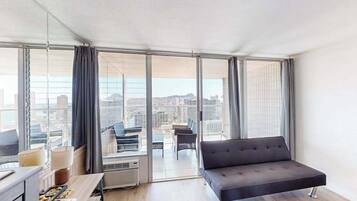Une chambre d’hôtel moderne, dotée d’un canapé, d’une table à manger et offrant une vue sur le paysage urbain grâce à de grandes fenêtres.