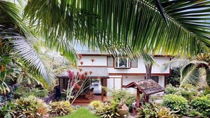 Una casa con patio coperto, circondata da piante tropicali rigogliose e un piccolo giardino.