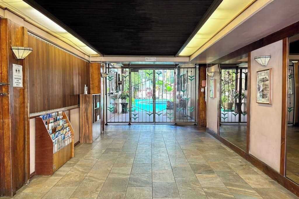 A hotel lobby with a reception desk, a tiled floor, and a view of a pool through glass doors.