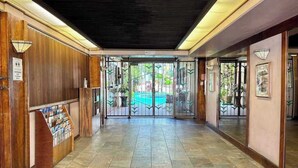Ein Hotel-Lobby mit einer Rezeption, einem gefliesten Boden und Blick auf einen Pool durch Glastüren.