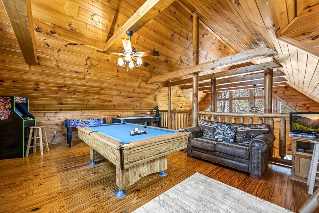 A wooden interior with a pool table, a sofa, and a television.