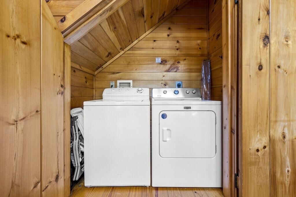 Ein kleiner Waschraum mit zwei weißen Waschmaschinen und Trocknern, Holzwänden und einer geneigten Decke.
