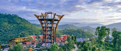A unique tower structure with multiple levels, surrounded by lush greenery and a mountainous backdrop.