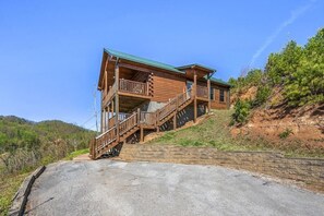 Uma cabana de madeira com varanda e escadas, localizada numa encosta sob um céu claro.