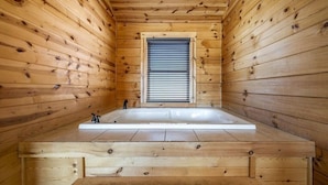 A wooden cabin interior with a large wooden bathtub, a window with blinds, and a wooden floor. - Brave Eagle (Gatlinburg)