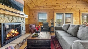 A cozy living room with a fireplace, a sofa, a chair, and a television mounted on the wall. - Brave Eagle (Gatlinburg)