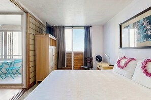 A hotel room with a bed, a desk, a chair, a balcony with blue chairs, and a large window with curtains. - Harbor View Plaza Condo Near Waikiki and Ala Moana, Pool, Kitchen, Balcony Views (Honolulu)