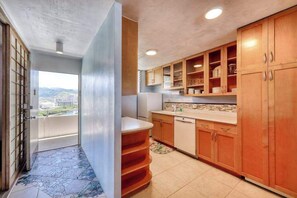 A kitchen with wooden cabinets, a countertop, and a view through an open door. - Harbor View Plaza Condo Near Waikiki and Ala Moana, Pool, Kitchen, Balcony Views (Honolulu)