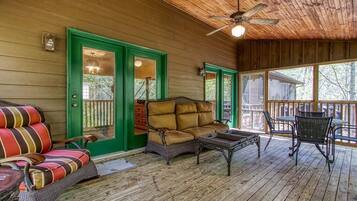 A covered porch with a wooden ceiling, a green door, a brown sofa, and a table with chairs.