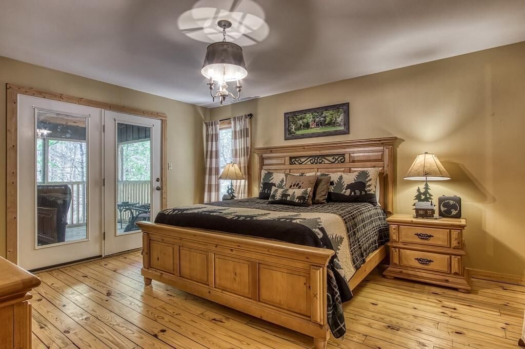 A bedroom with a wooden bed, a ceiling fan, a nightstand with a lamp, and a window with curtains.
