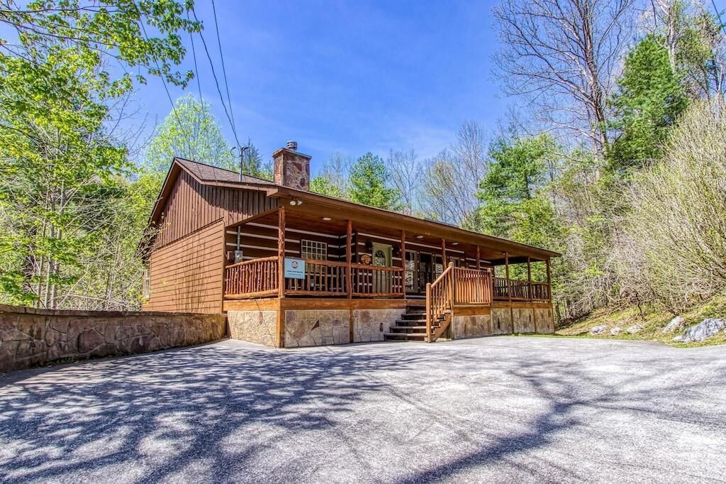 A wooden cabin with a porch, stone foundation, and a clear sky.