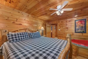 A wooden cabin room with a bed, a ceiling fan, a painting, and a red bathtub. - Can't Bear to Leave (Sevierville)