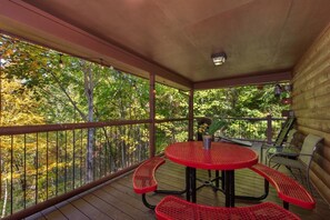 A covered outdoor area with a table and chairs, surrounded by a wooden deck and a metal railing. - Can't Bear to Leave (Sevierville)