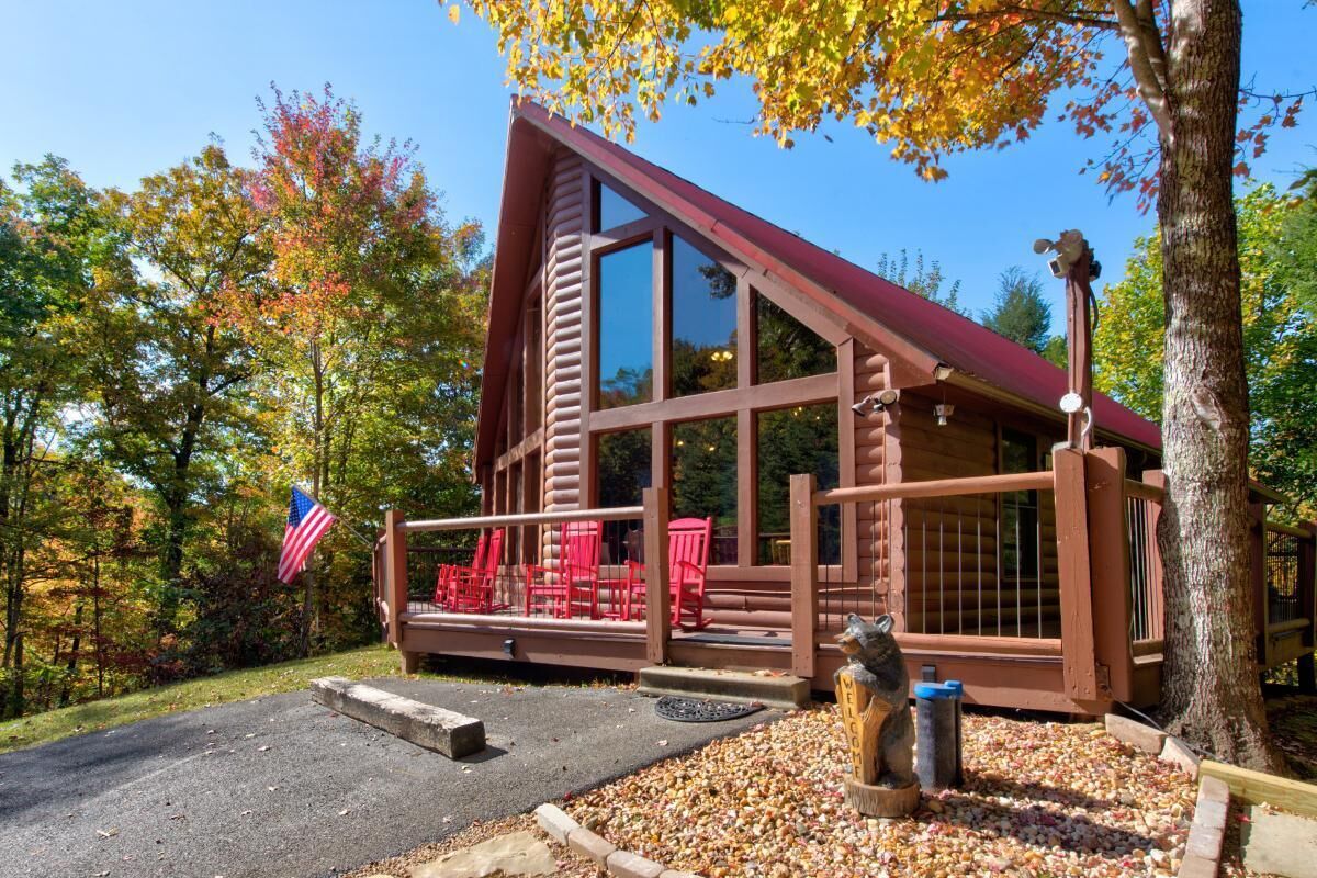 A cabin with a large window, a porch with red chairs, and an American flag.