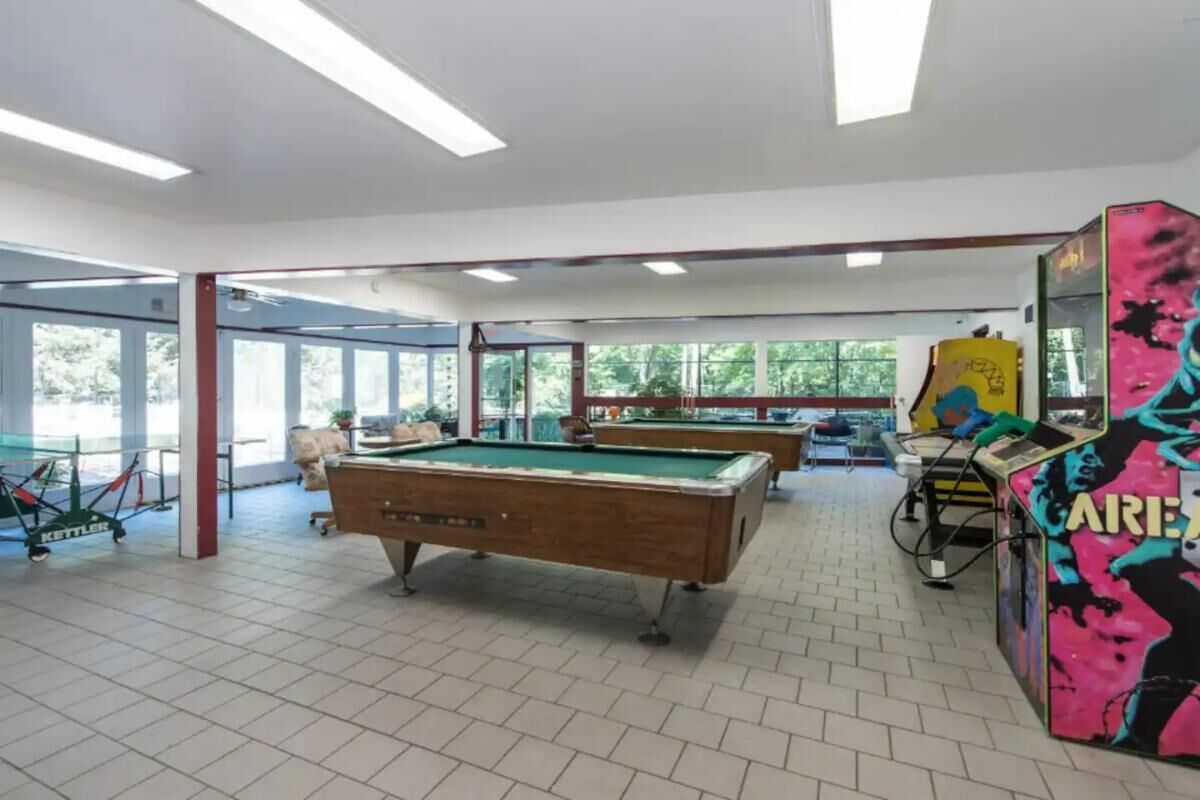 Ein Billardtisch in einem Raum mit großen Fenstern, ein Tischfußballautomat und eine farbenfrohe Spielmaschine.
