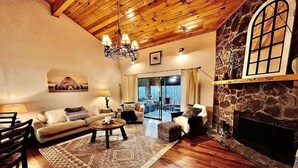 A cozy living room with a stone fireplace, wooden ceiling, and a large window. - Chalet in the Smokies (Gatlinburg)