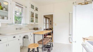 A kitchen with white cabinets, a wooden countertop, a metal stool, and a refrigerator. - *New* Two Waikiki Cottages with Diamond Head Views | 30 Nights (Honolulu)