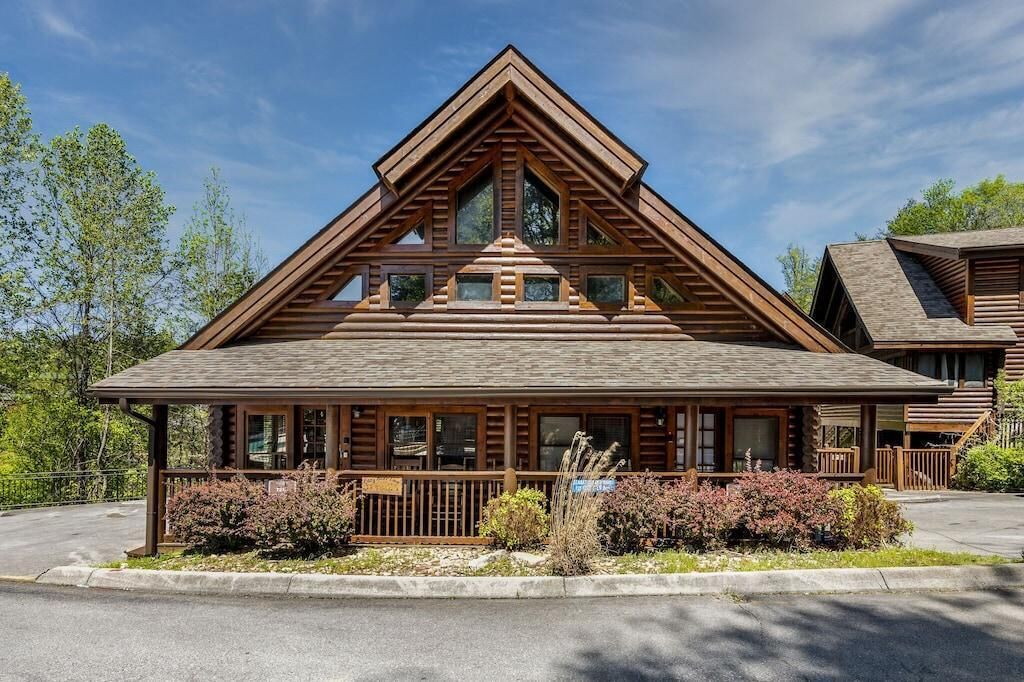 A log cabin-style building with a prominent triangular roof, large windows, and a covered porch area.