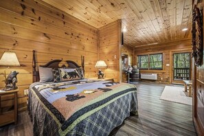 A wooden cabin room with a bed, two bedside lamps, a nightstand, a large window, and a rustic decor. - Cozy Bear Cove (Pigeon Forge)