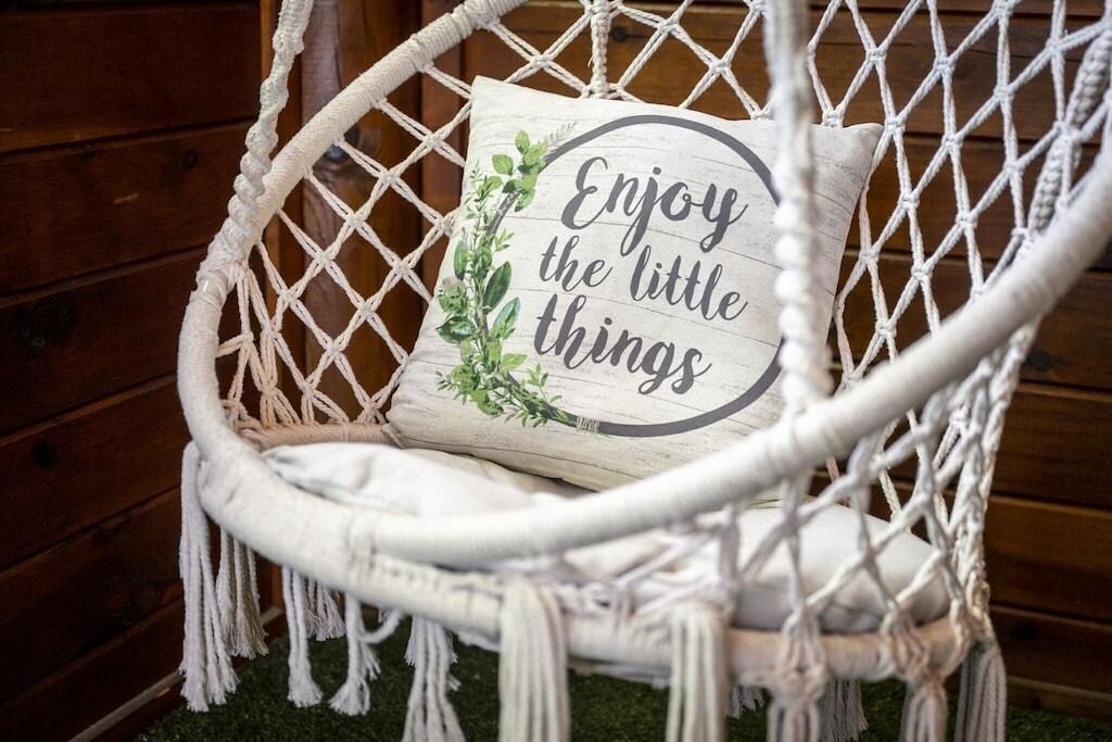 Un fauteuil en macramé agrémenté d’un coussin sur lequel est brodé le message : « Savourez les petits plaisirs de la vie. »