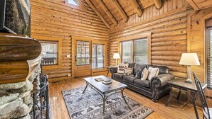 A log cabin interior with a fireplace, a sofa, a coffee table, and a dining area. - Cozy Bear Cove (Pigeon Forge)