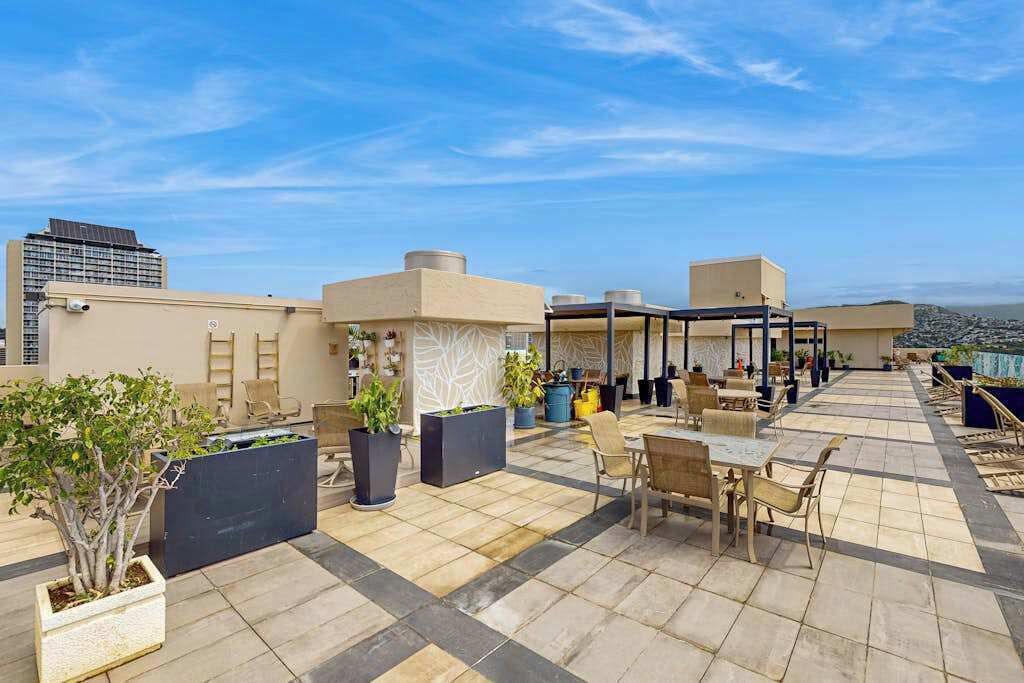 Eine Dachterrasse mit Sitzgelegenheiten im Freien, Pflanzgefäßen und Blick auf die Stadt.
