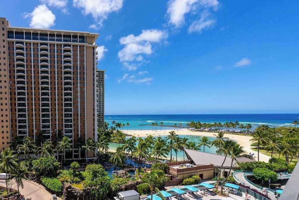 Ein Hochhotel mit Blick auf den Strand, einem Poolbereich und wolkenlosem, blauem Himmel.