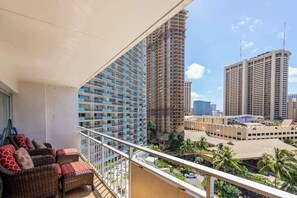 A balcony with wicker furniture, high-rise buildings in the background, and a clear sky. - *NEW* Ocean-and-City Views Near Kahanamoku Beach (Honolulu)