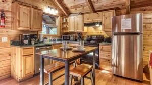 A wooden cabin interior with a kitchen area featuring a stainless steel refrigerator, wooden cabinets, a dining table with benches, and a microwave. - Cozy Bear Lodge (Sevierville)
