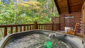 A hot tub with a wooden deck and a view of a forest. - Cozy Bear Lodge (Sevierville)
