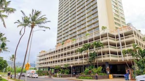 Un hôtel à plusieurs étages, doté d’un design moderne, avec une entrée imposante abritée et un parking visible au premier plan.