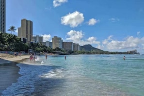 A beach with clear water, palm trees, and high-rise buildings in the background. - Waikiki High Rise Studio - 30 night minimum (Honolulu)