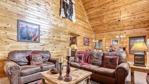 A cozy cabin interior with wooden walls, leather sofas, a wooden coffee table, and framed pictures. - Cubs Cozy Den (Sevierville)