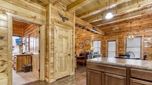 A wooden cabin interior with a kitchen area, a dining table, and a fireplace. - Eagle's Hangout (Sevierville)
