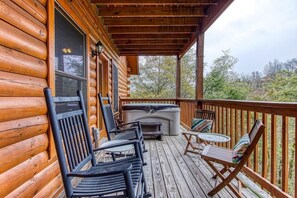 A wooden deck with outdoor seating, a hot tub, and a view of trees. - Eagle's Hangout (Sevierville)