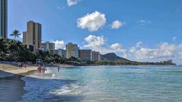 Ein Strand mit klarem Wasser, Palmen und Hochhäusern im Hintergrund.