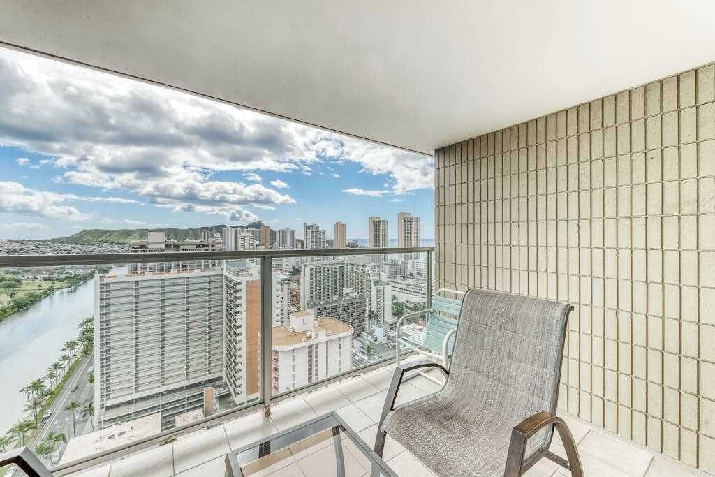 A balcony with a city view, a chair, and a glass table.