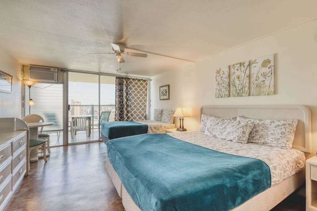 A bedroom with a bed, a desk, a chair, and a window with a view.