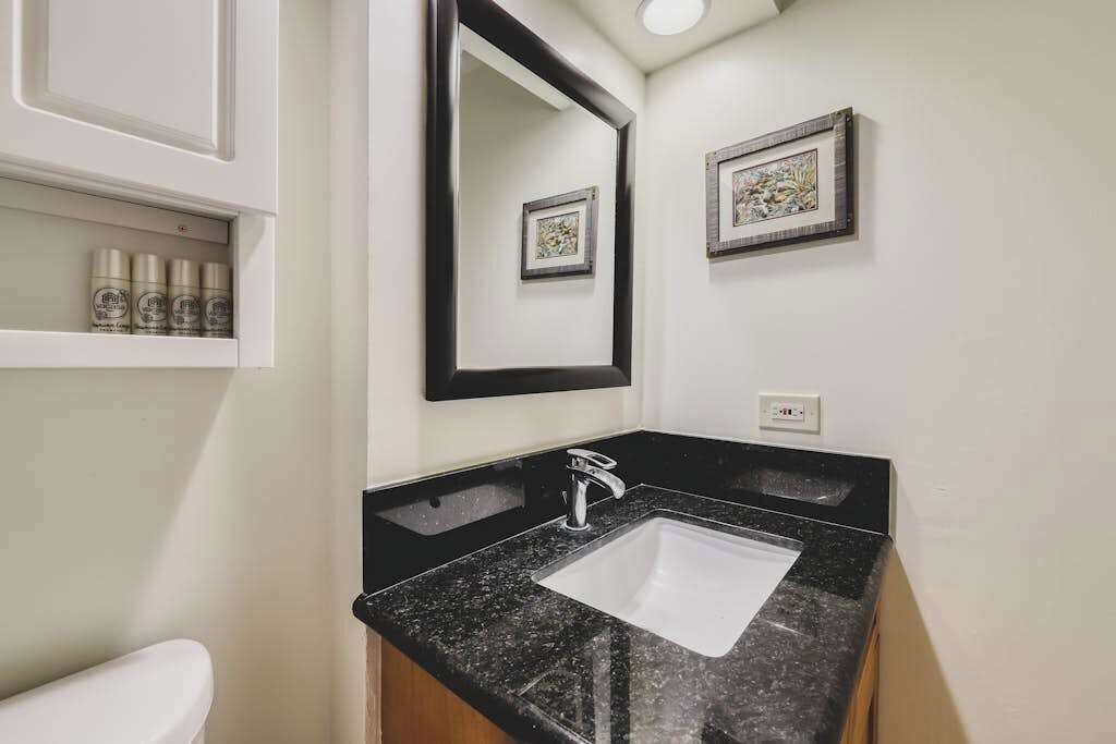 A bathroom with a black granite countertop, a white sink, a mirror, and framed artwork on the wall.