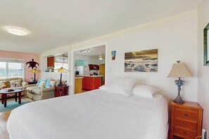 Un dormitorio con cama, mesita de noche, lámpara, un cuadro y vistas a la cocina.
