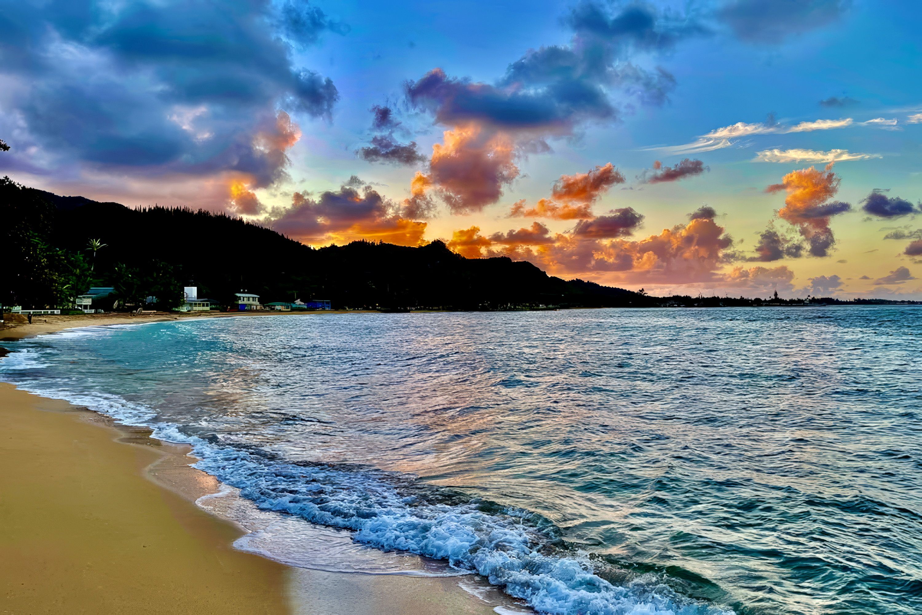 A beach with waves, a sunset, and a mountain in the background.