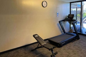 A treadmill, a bench, a clock, and a window with a view of buildings. - New Fall $ale Waikiki Studio with City-View Balcony One Block from the Beach (Honolulu)