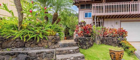 A residential property with a stone staircase, a balcony, and a well-maintained garden with various plants and a decorative pot.