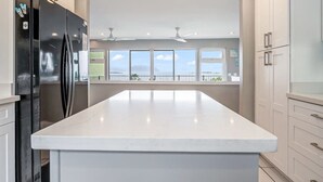 Una cucina con una grande isola, un frigorifero nero, mobili bianchi e vista dalle finestre.