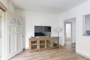 A hallway with a wooden cabinet, a television, and a door with a semi-circular window. - New Garden-Quiet Honolulu Guest House with Mountain Views (Honolulu)