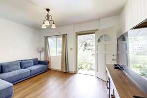 A modern living room with a sofa, wooden flooring, a ceiling light fixture, and a door leading to an outdoor area. - New Garden-Quiet Honolulu Guest House with Mountain Views (Honolulu)