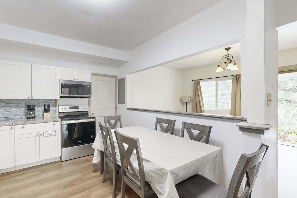 Una cocina moderna con armarios blancos, microondas, estufa y una mesa de comedor con sillas.
