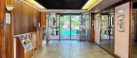 Un hall d’hôtel avec un comptoir d’accueil, un sol carrelé et une porte vitrée donnant sur l’extérieur.