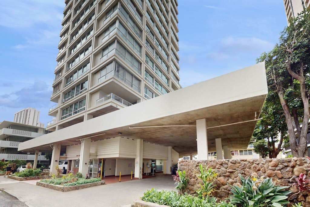 A modern building with a covered entrance, a stone wall, and a landscaped area with plants.