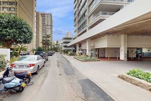 A street with parked cars and a building with a covered parking area. - Waikiki High Rise - 30 night minimum (Honolulu)